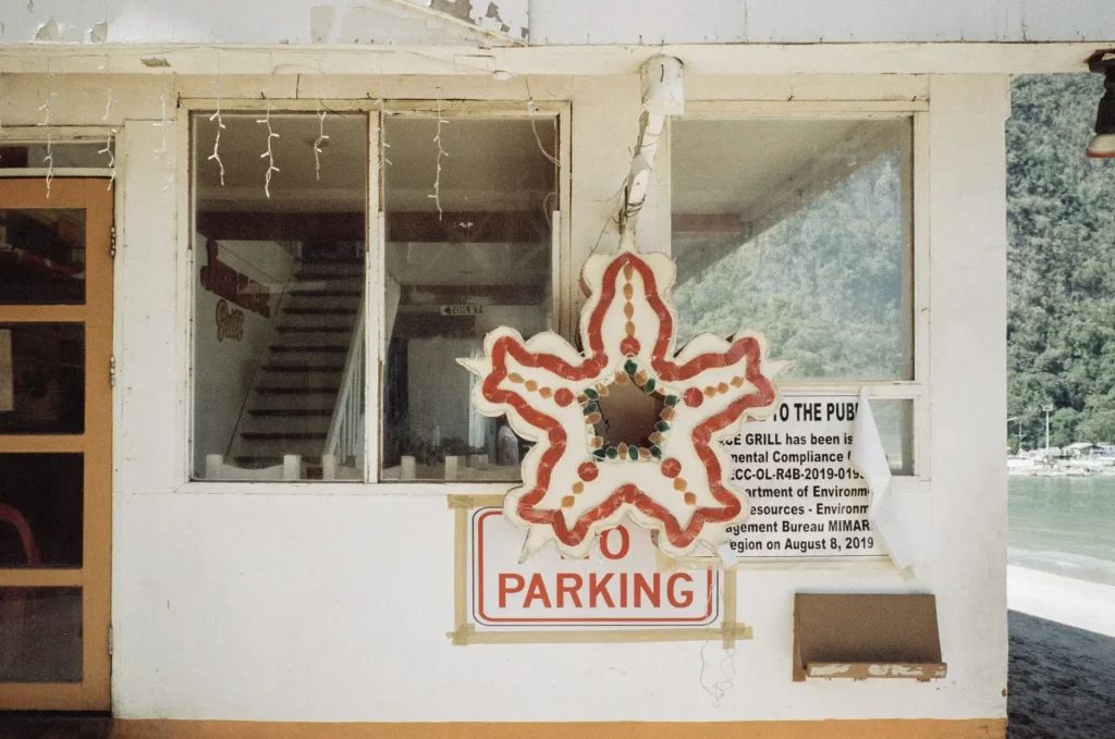 A decorative star ornament hangs on a white concrete building, partially obscuring a sign that reads 'NO PARKING'.