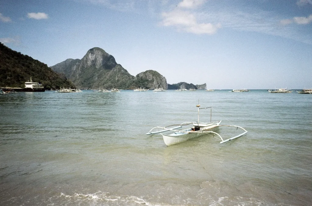 A boat sits passenger-less in a brigth blue ocean with mountains in close distance.