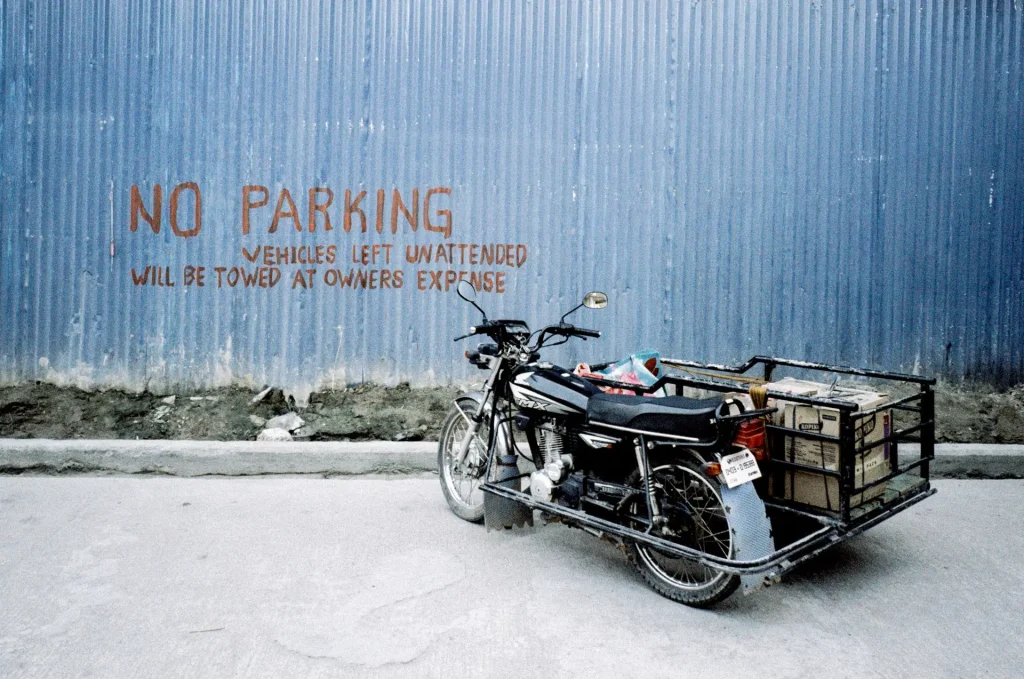 A motorcycle sits parked in front of a blue metal wall with the words 'NO PARKING' written in red.