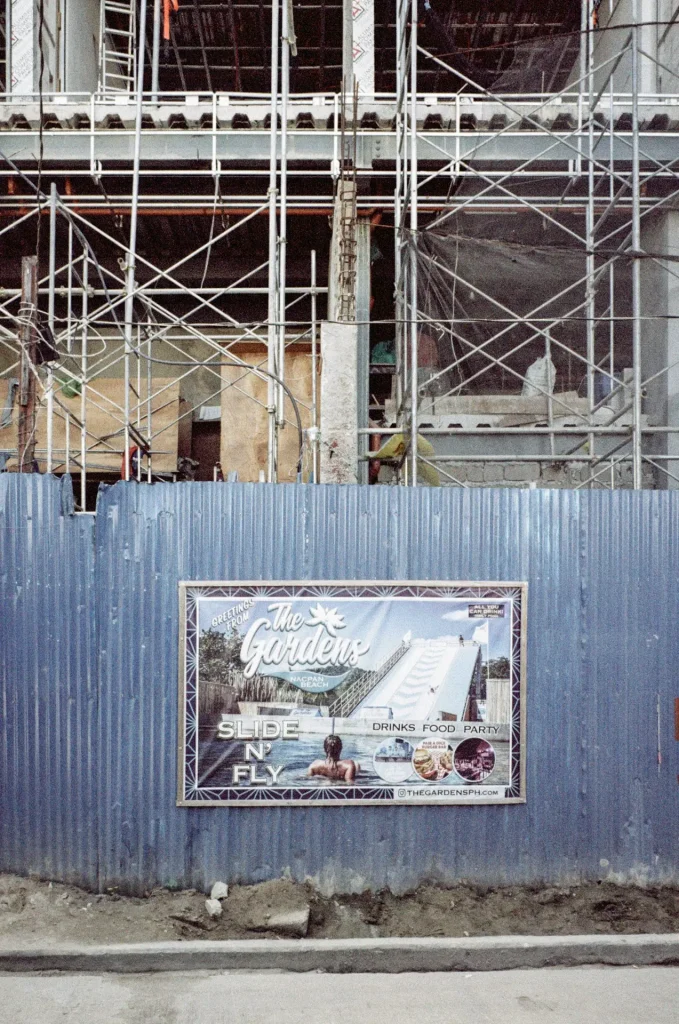 A blue metal wall sits in front of a construction site with a poster promoting a forthcoming waterslide park's future debut.