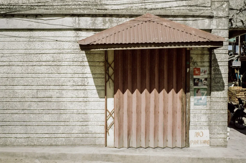 A ridged brown door with a brown canopy sits flush in a gray concrete wall.