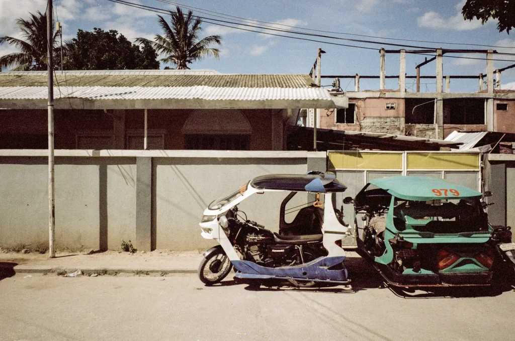A white & green tuk-tuk rickshaw parked in front of a gray concrete building.