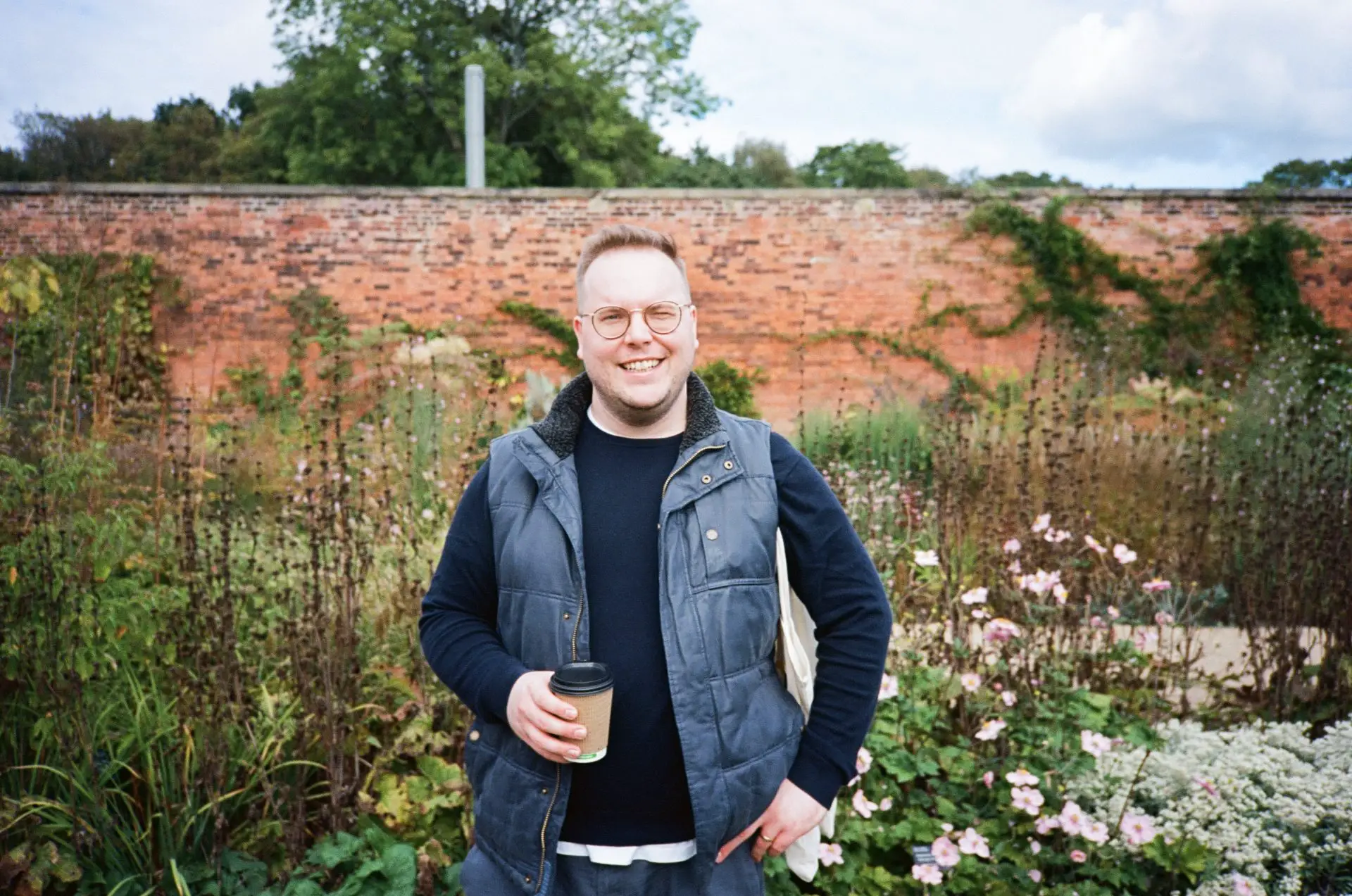 I'm stood in the centre of the frame holding a cup of coffee in front a large bed of mixed decorative plants.