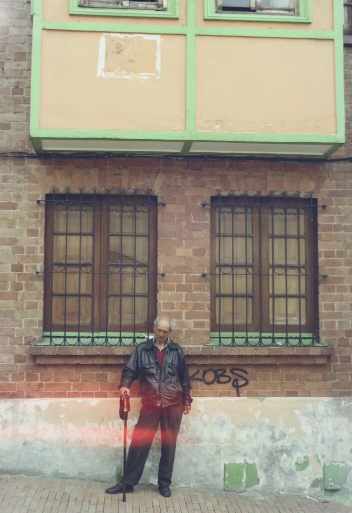 An older resident of Bogota leans against a building with a swagger, using a cane in his right hand.