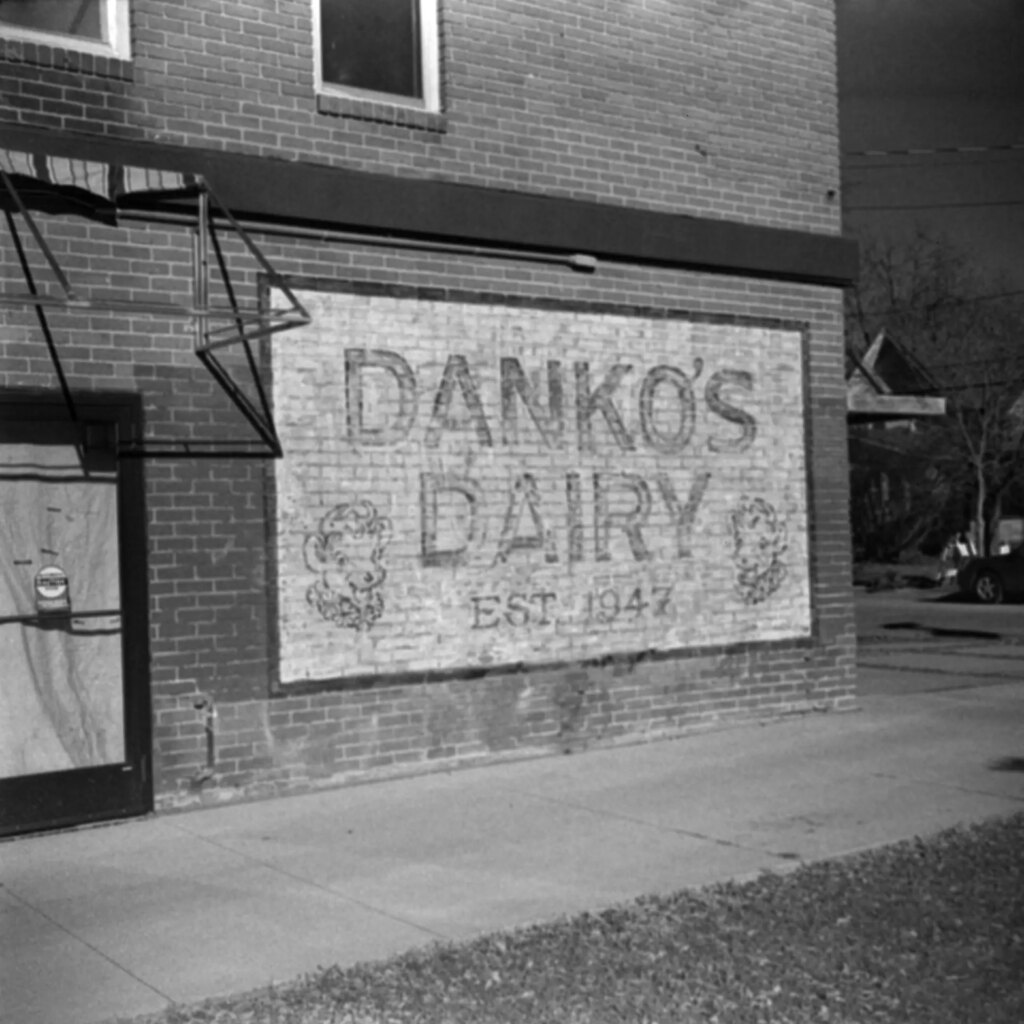 A black-and-white photo of a mural painted on the side of a brick building. The mural reads "Danko's Dairy Established 1947"