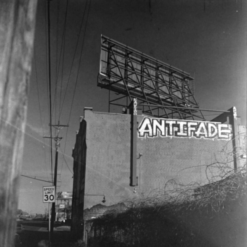 A black-and-white photo of the back of a brick building. Painted on the building's wall in graffiti is the word "Antifade"