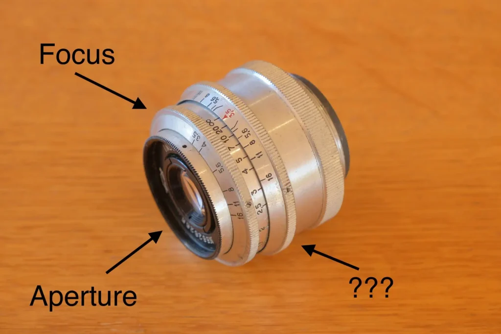 The lens, with the aperture ring, focus ring, and immobile mystery ring labeled.