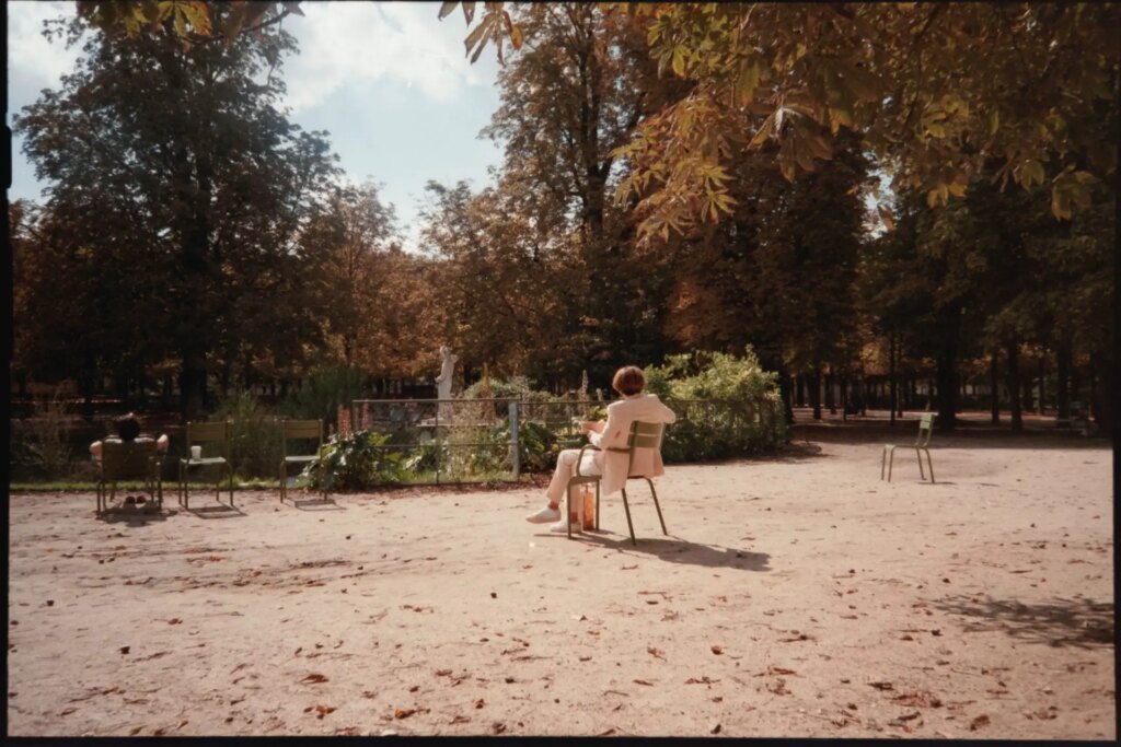 a lady dressed in all beige, sitted in a chair, reading a book and enjoying the sun in the Jardin du Luxembourg