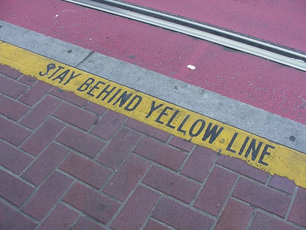 Pavement with a "Stay Behind Yellow Line" warning