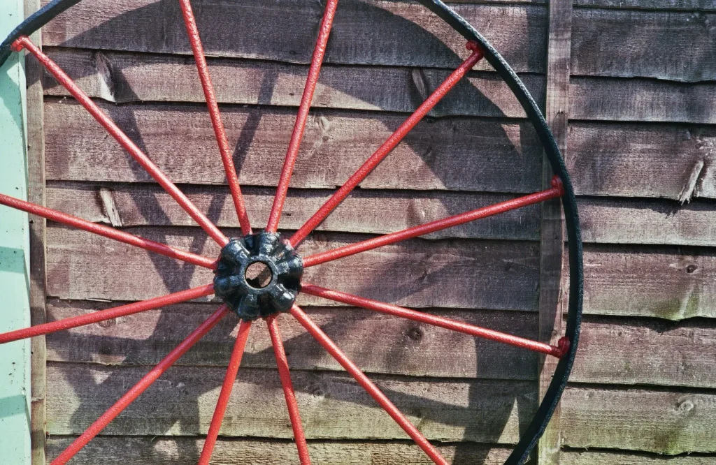 Red Waggon wheel in front of fence