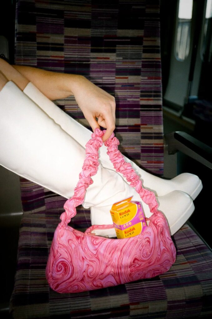 Alex Heron holding her pink purse with film and white boots on the Elizabeth line