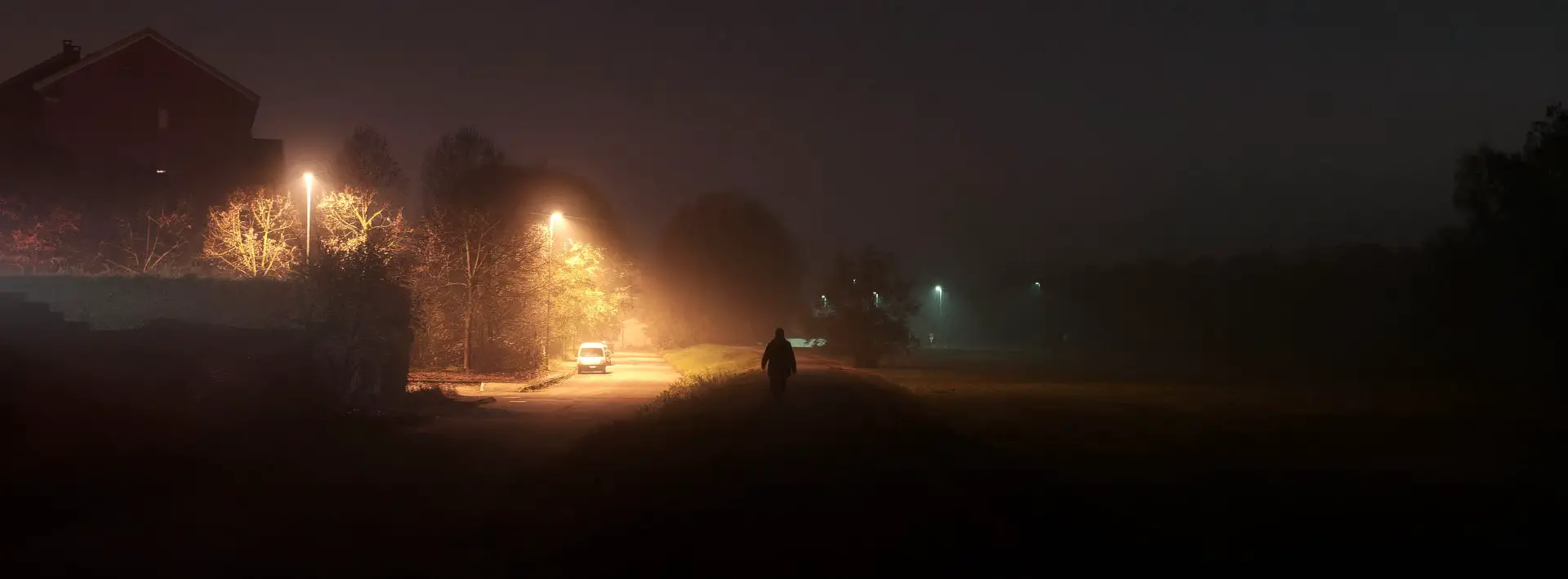 A man walking in the dark, lighten up only by a street light coming from above.