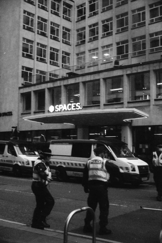 Two police in front of two police vans and a store.