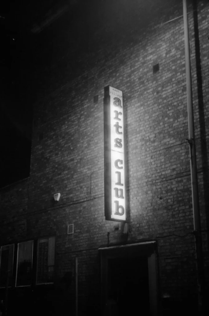 A large illuminated sign saying "East Village Arts Club".
