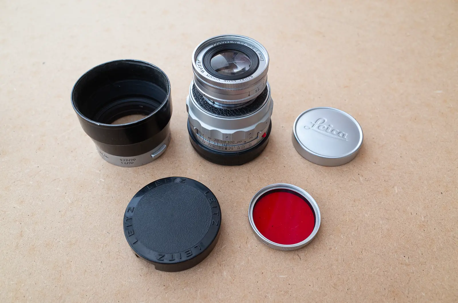 Elmar 9cm f/4 collapsed, IUFOO hood and compatible cap, A39 slip-on cap, and a 39mm R (red) Leitz filter