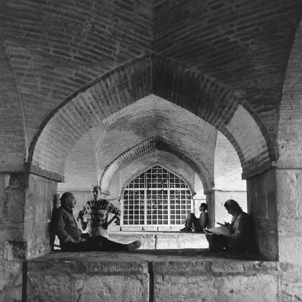 A man sitting under an arch and singing. Other people also sit there reading or listening.