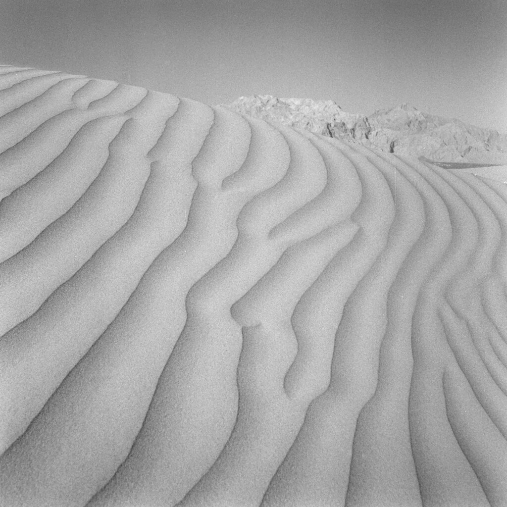 A sand dune on a desert with mountains in the distance