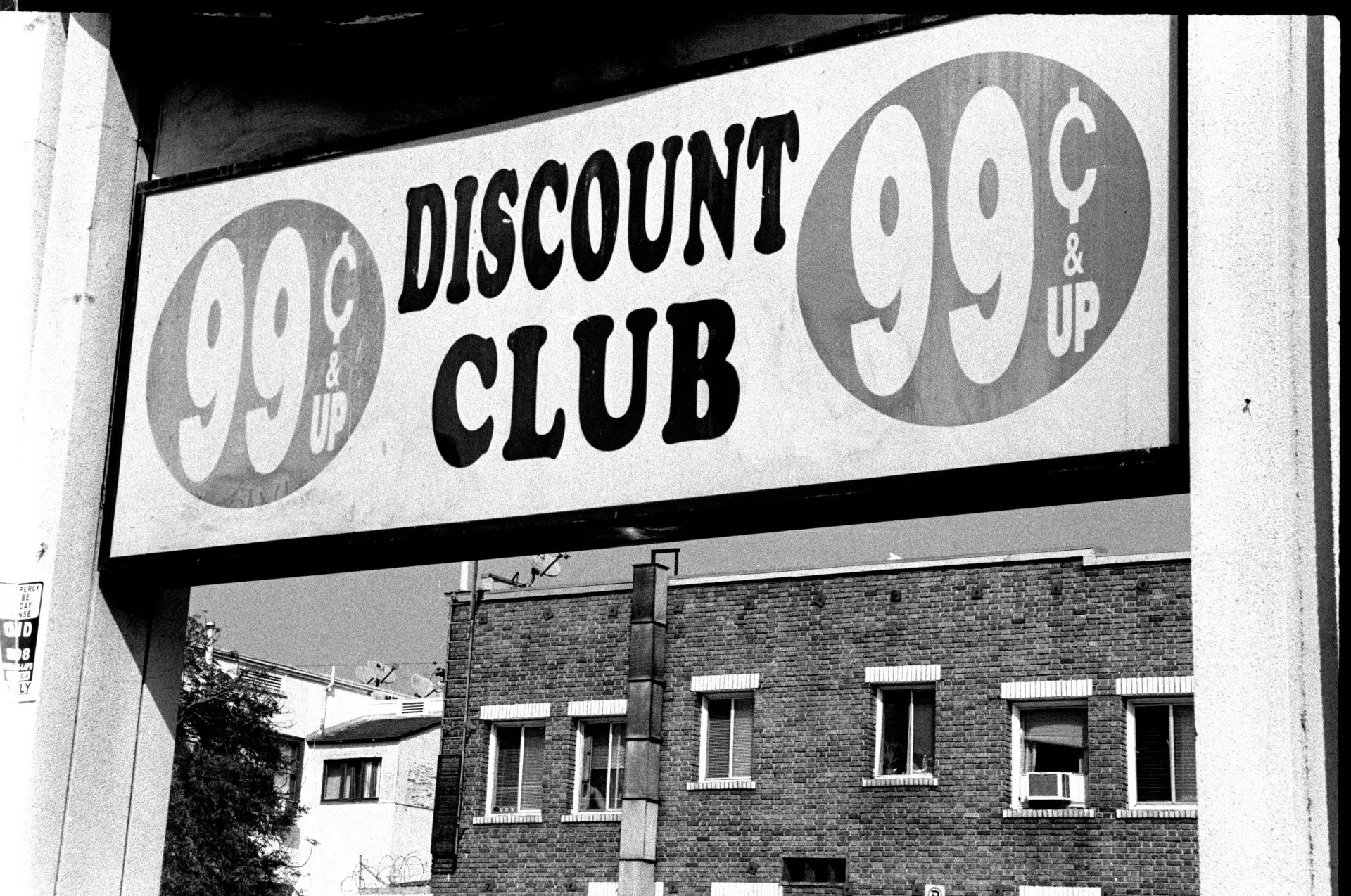 A sign reading "99 cents & up DISCOUNT CLUB", with a brick building behind it.