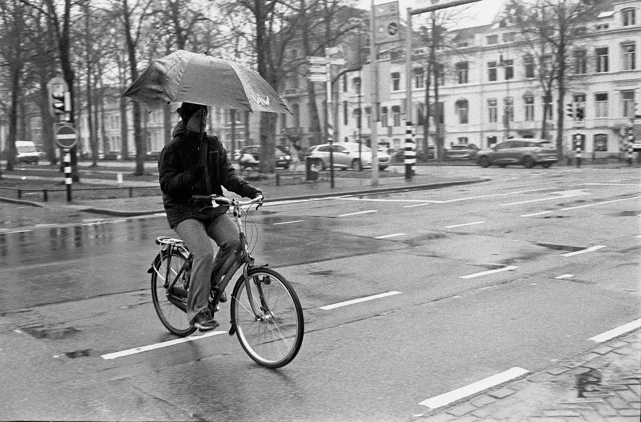 Man riding bike in rain holding an umbrella.