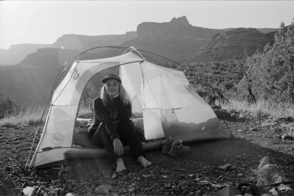 black and white photograph of a woman sitting in a tent in early morning light with mountains in the background