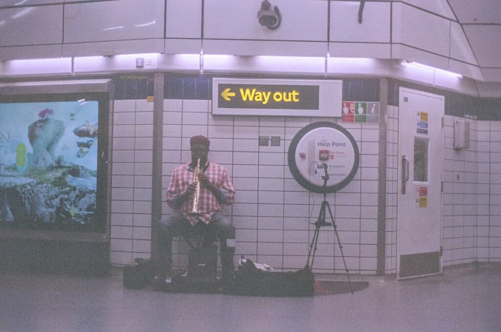 A busker playing in the London Underground with a Way Out sign above his head.