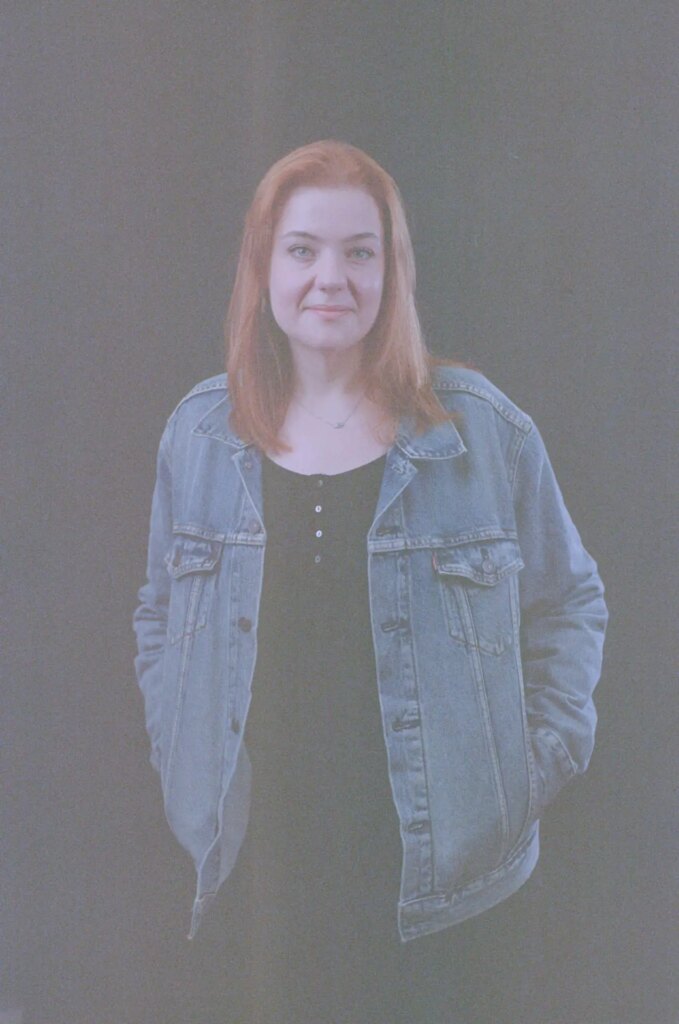 Studio portrait of a female with red hair, wearing a denim jacket.