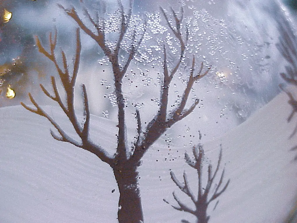 Detail of a Christmas ornament showing a bare tree in a snowy landscape