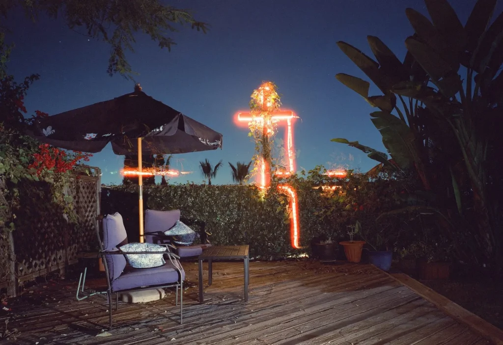Double exposure of a lit cross above a back yard patio.