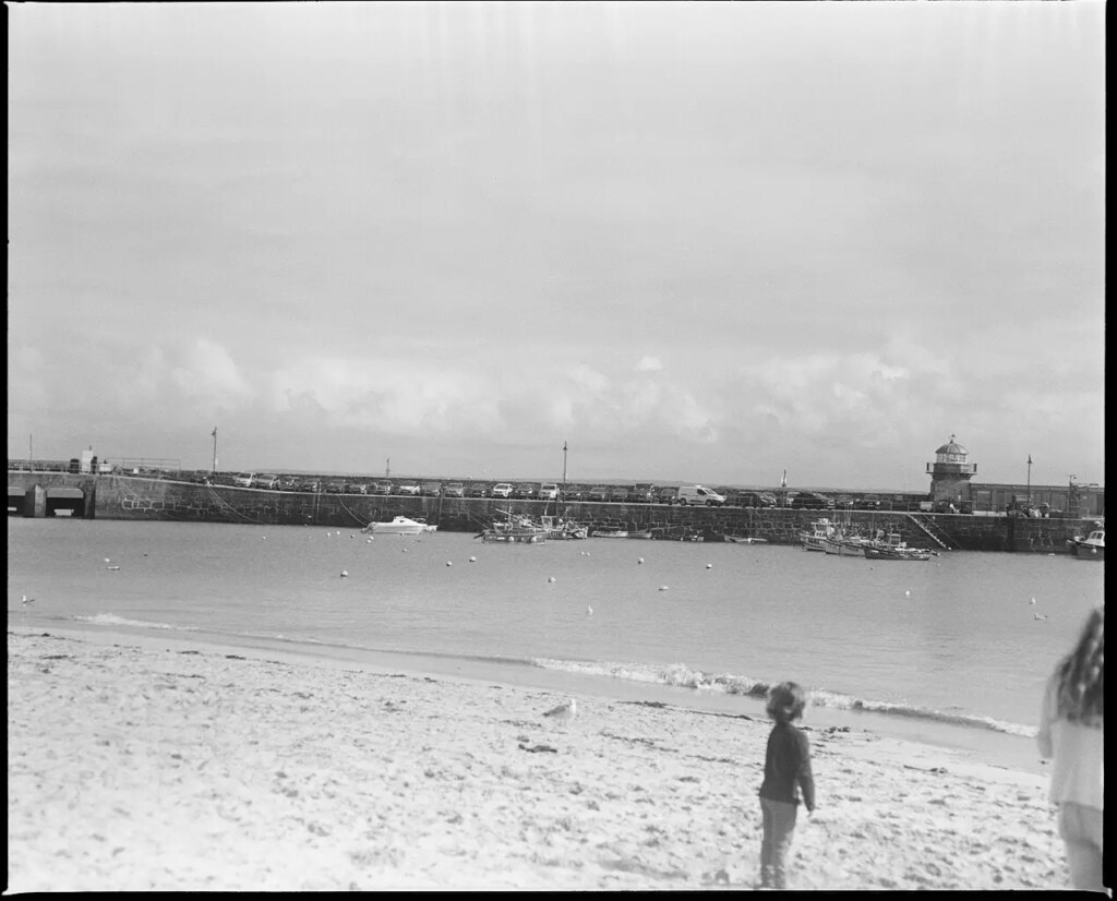 A child standing on a beach with another person almost in frame 