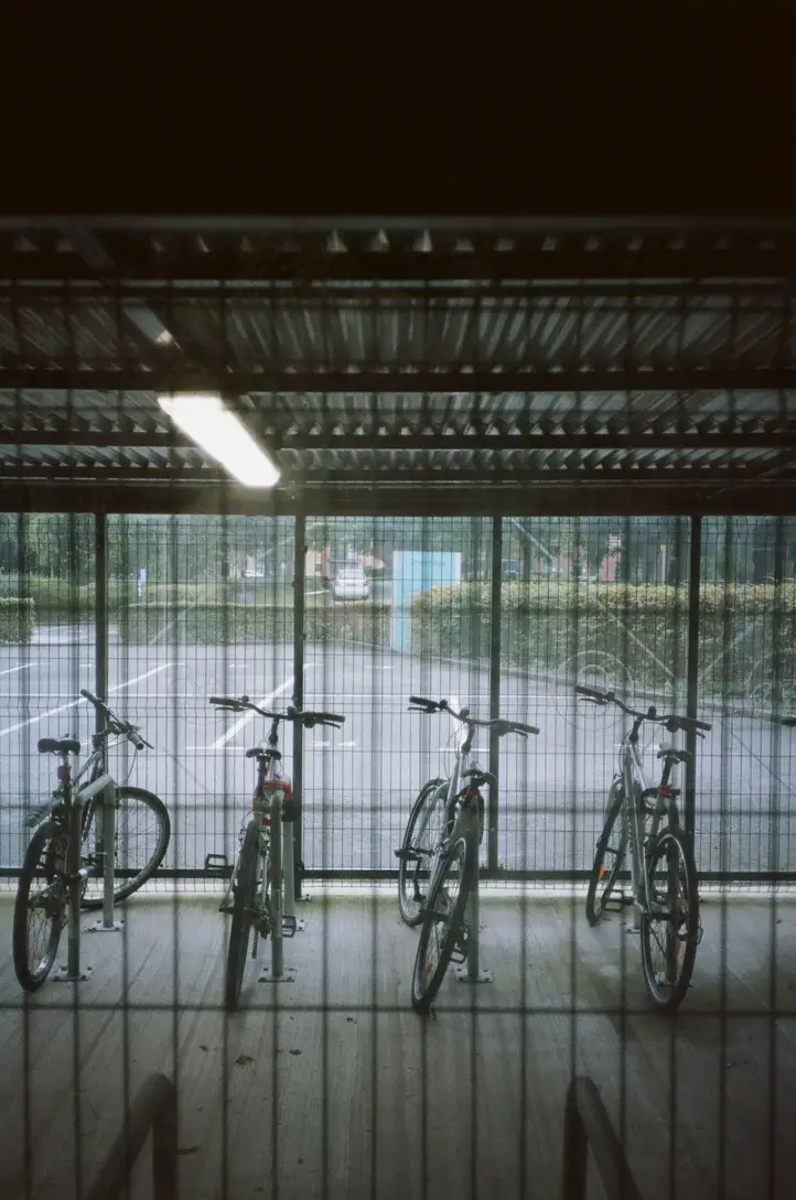 Four Bikes underneath a fluorescent light, image taken through glass and mesh, the background car park is dimly lit