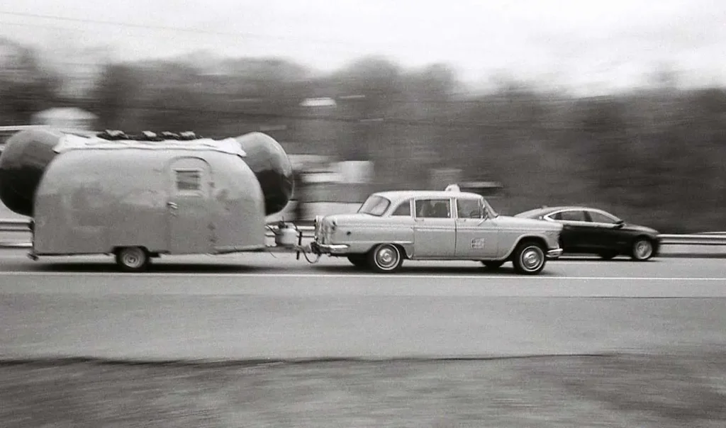 Car and Hot Dog trailer in traffic.