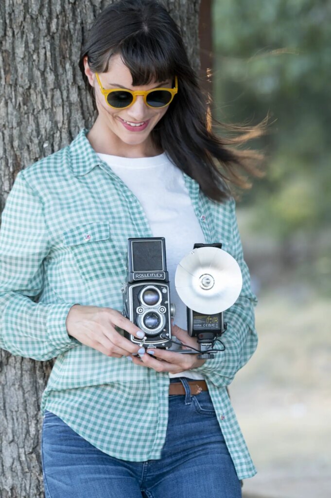 Woman leaning on tree outside holding rolliflex tlr camera with Lux Senior attached about to press the shutter button