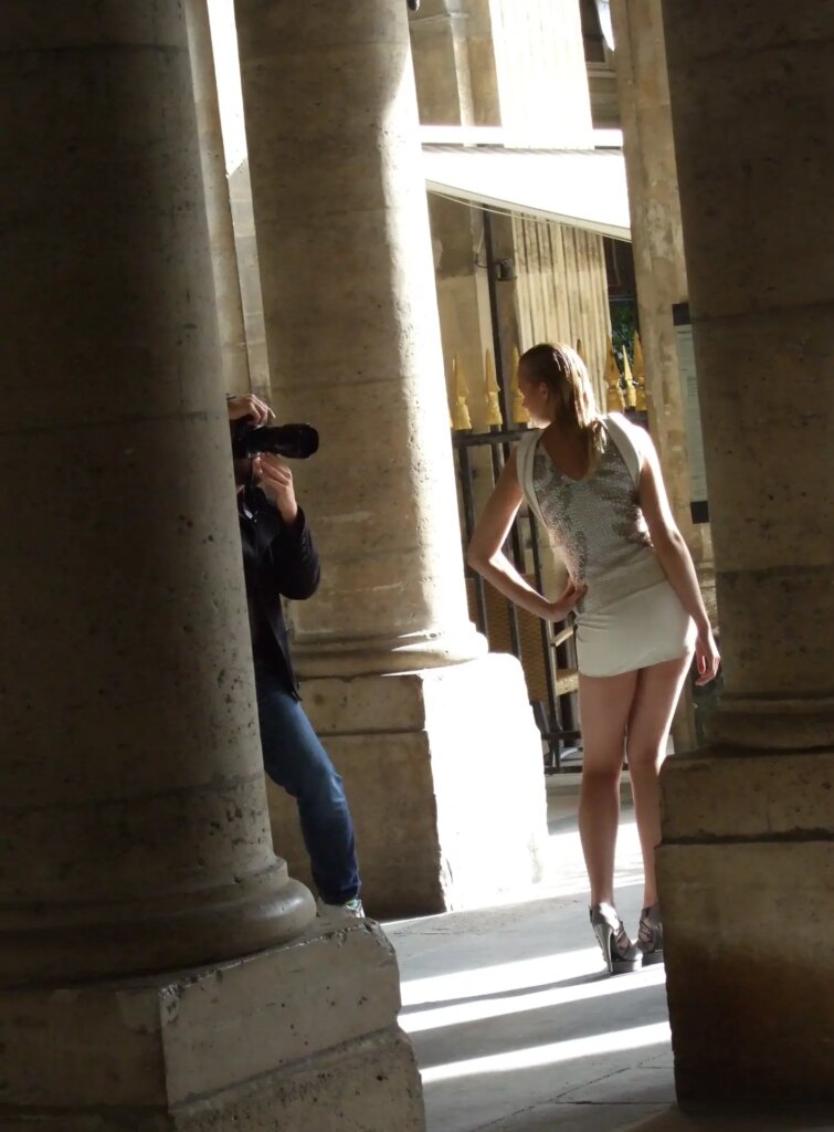 A photographer and his model, surrounded by building columns. 