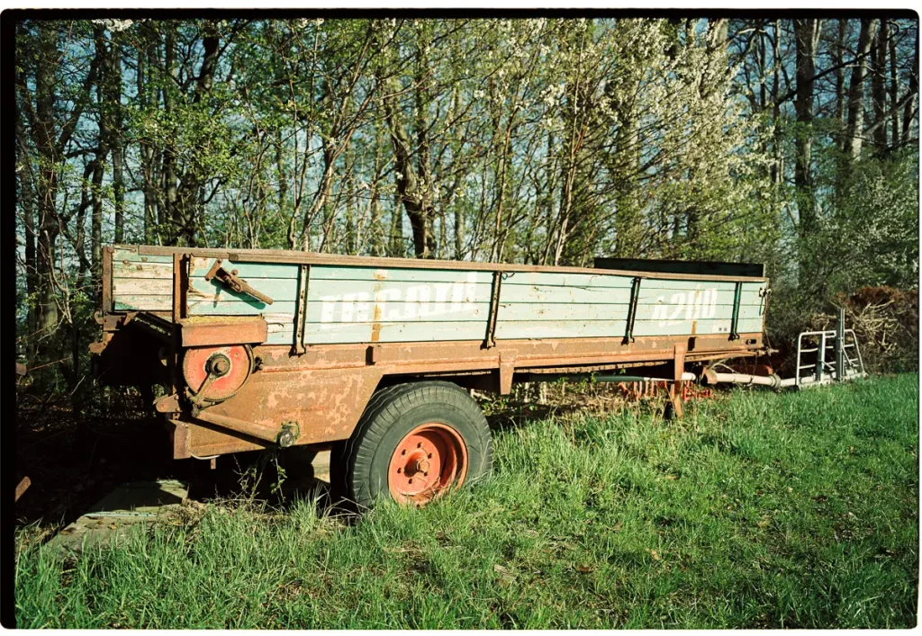 An old farming trailer stands at the edge of a woods.