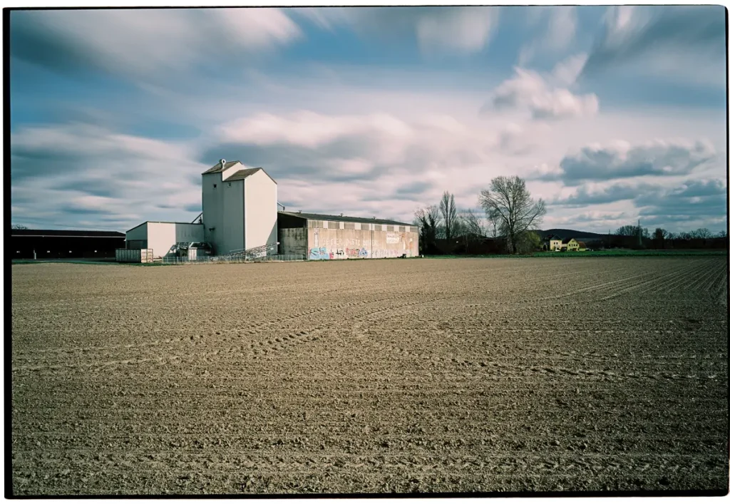 An agricultural warehouse is visible in the distance. Above the scene spans a dramatic sky; condensing time is again achieved by smeared clouds.