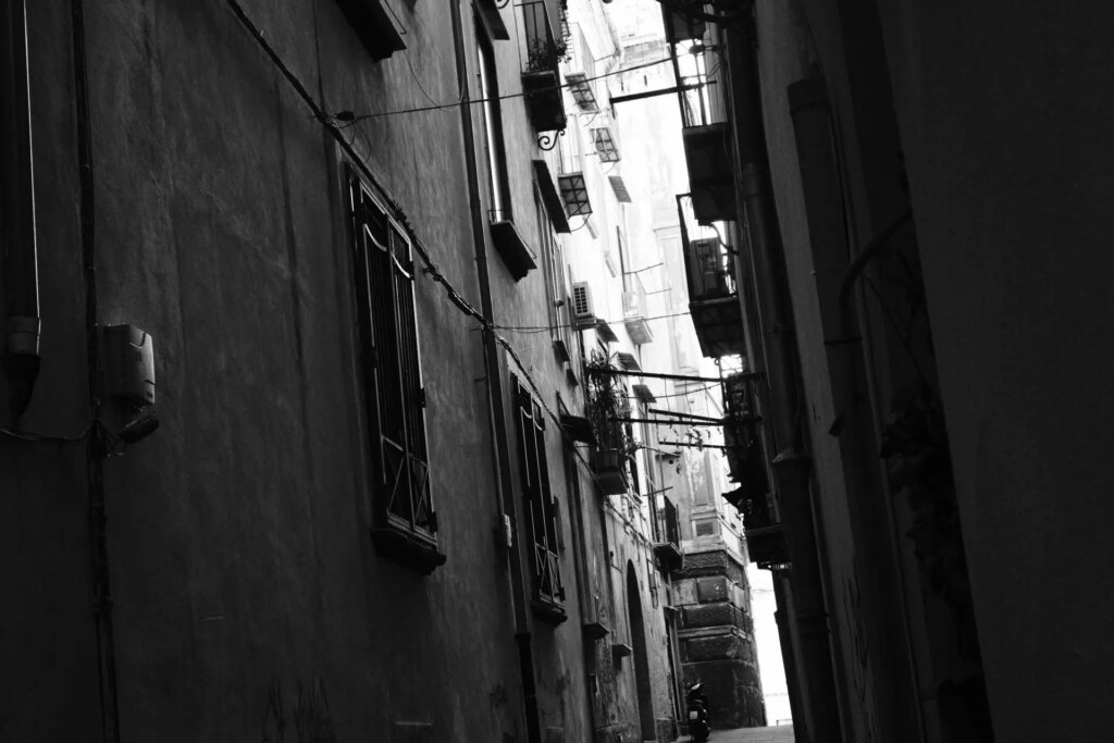 A dark, very tall, very narrow alley in Napoli. The sun is shining out from somewhere, creating a strong contrast, and lots of glow.
