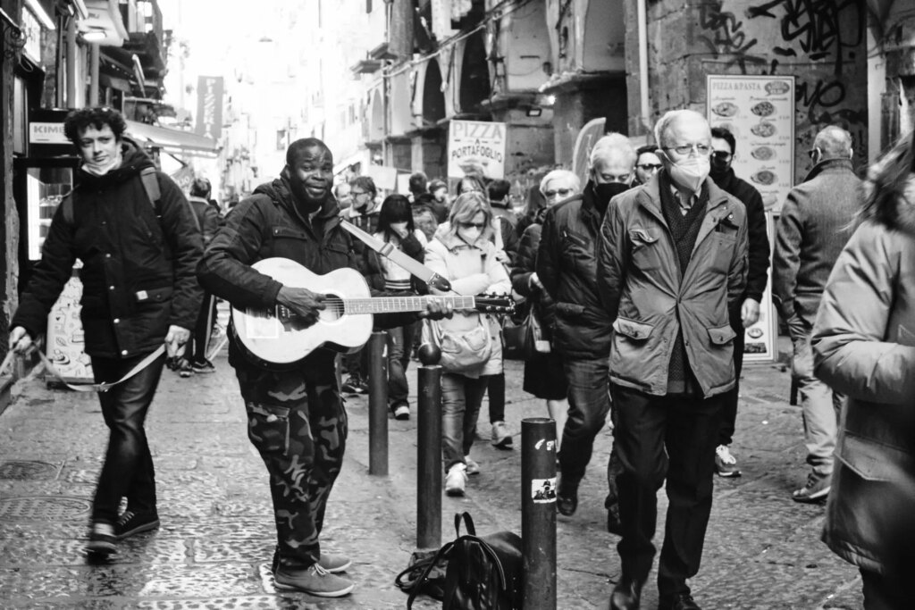 A street guitarist sings in falsetto for passers-by.