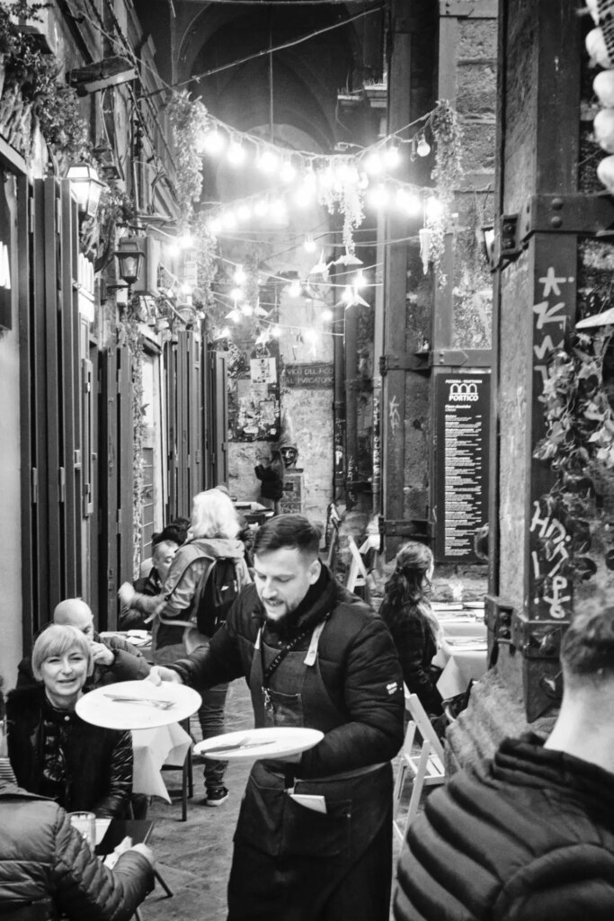 A pizzaiolo hurriedly clears plates from a table.