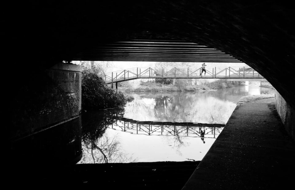 A jogger running over a canal on a cold morning