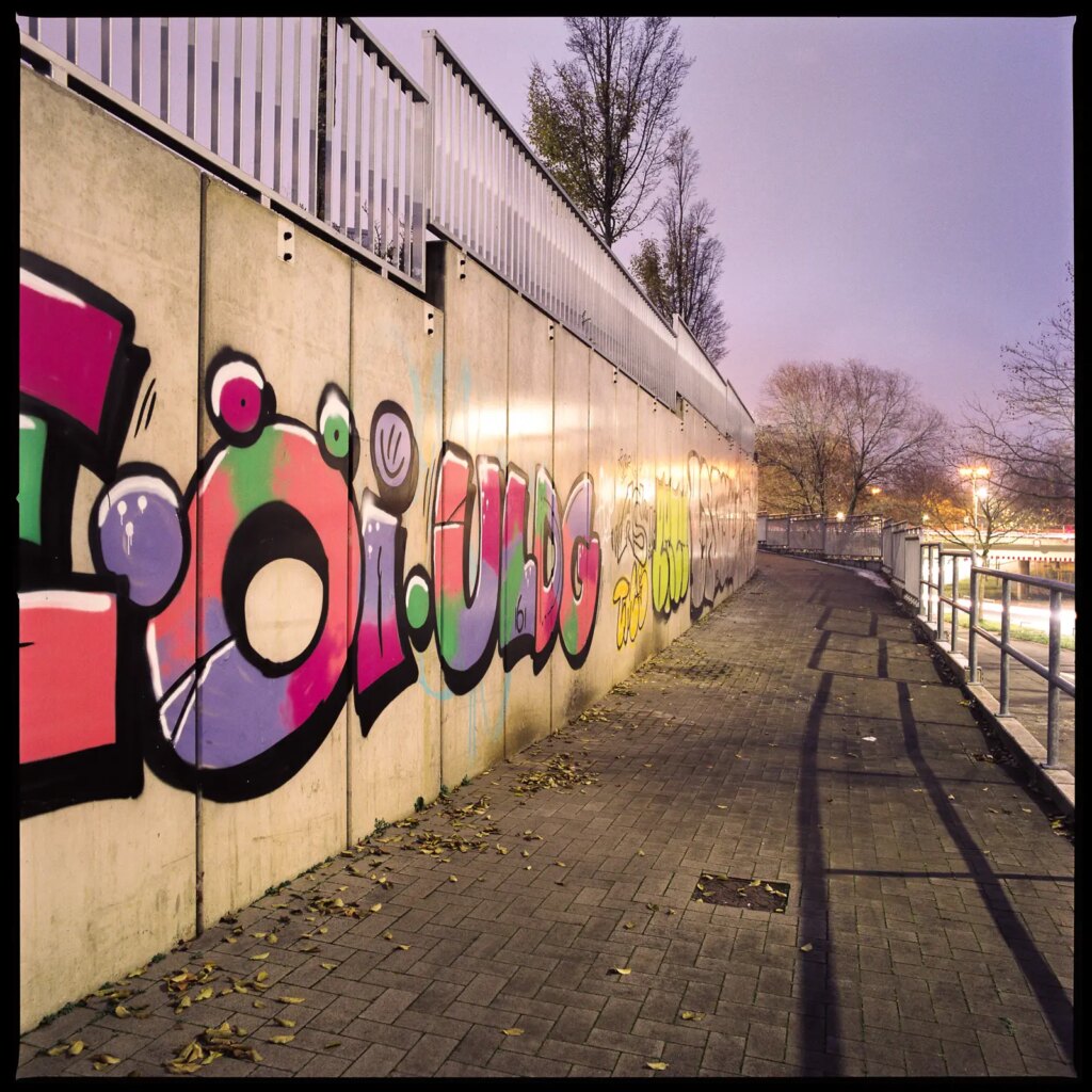 wide-angle medium format photograph showing a concrete wall covered with graffiti at night, shot with a Hasselblad Distagon 50mm f/4 lens