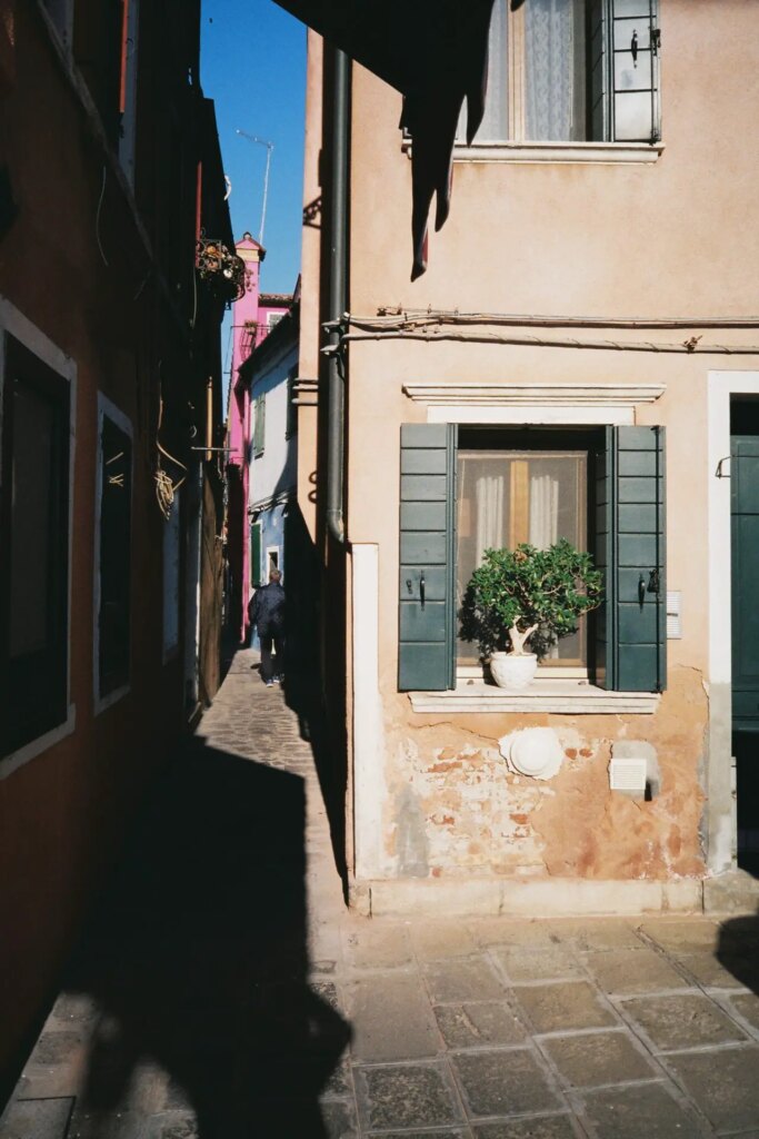 corner of a streets, in the shadows, somebody walking in the background.