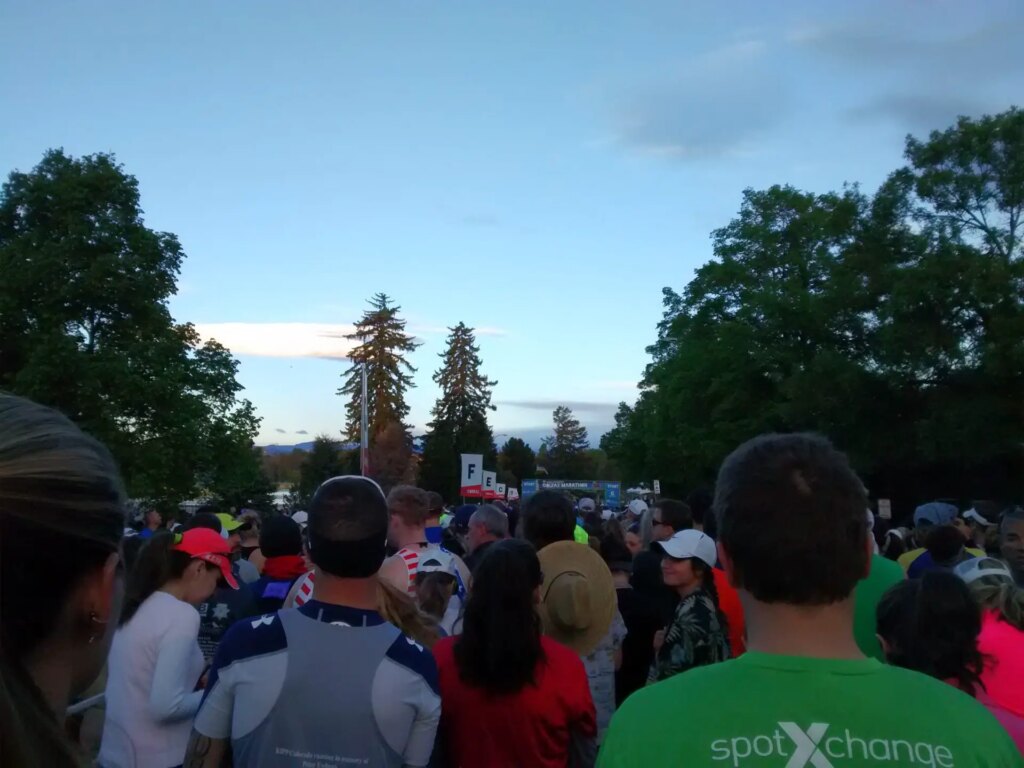 backs of lots of people's head at the starting line of a race clouds, trees, and early sky visible in background of photo