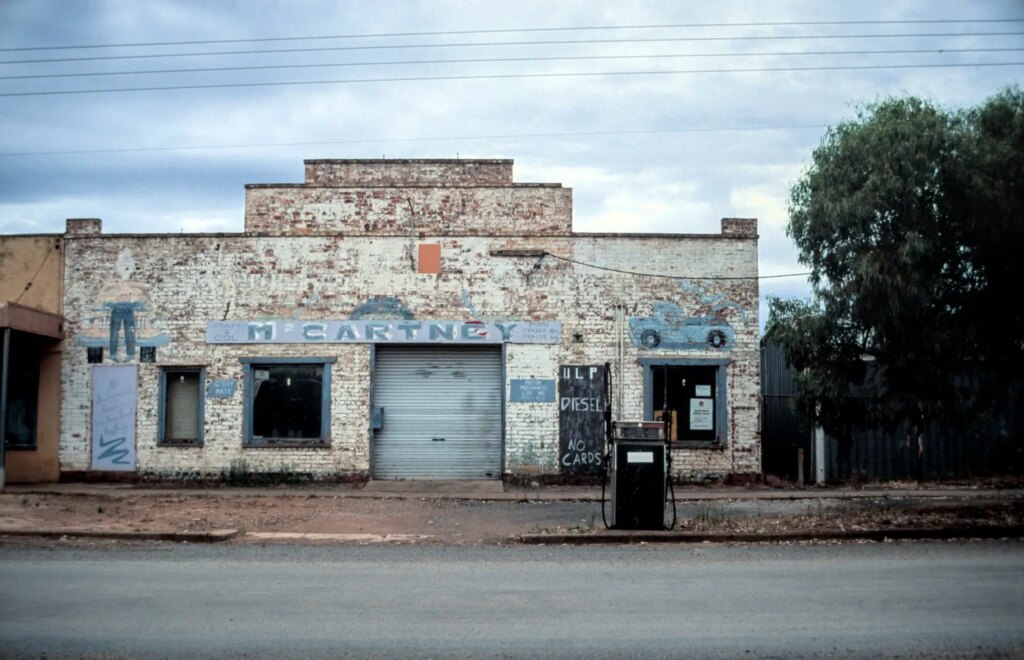 a while mechanics garage with faded and pealing pant. A single fuel bowser stands unused and rusting at the front 