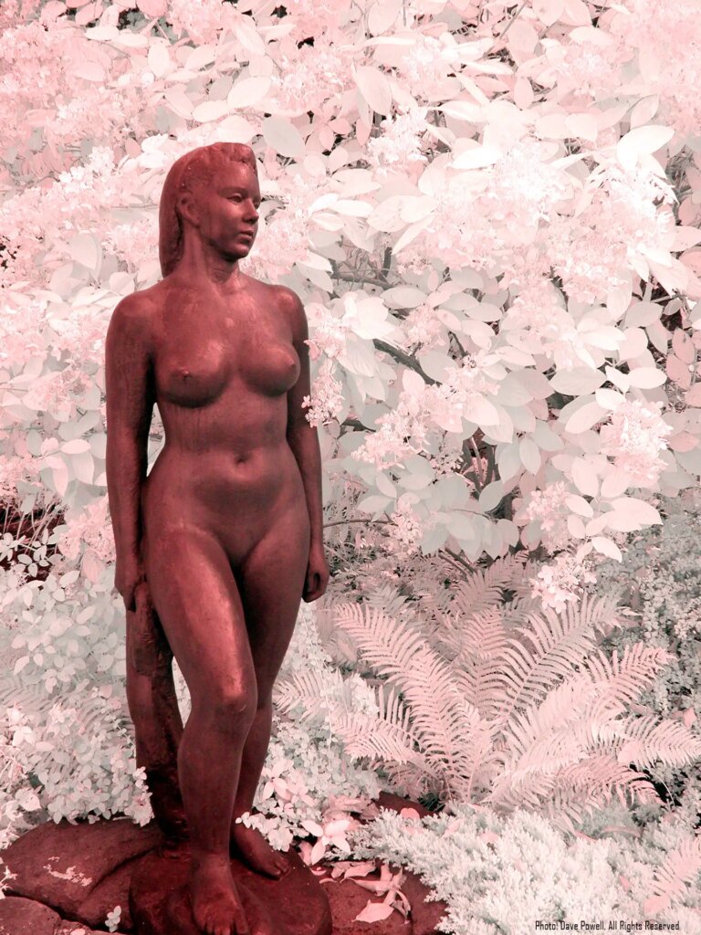 Bronze female statue in front of bush