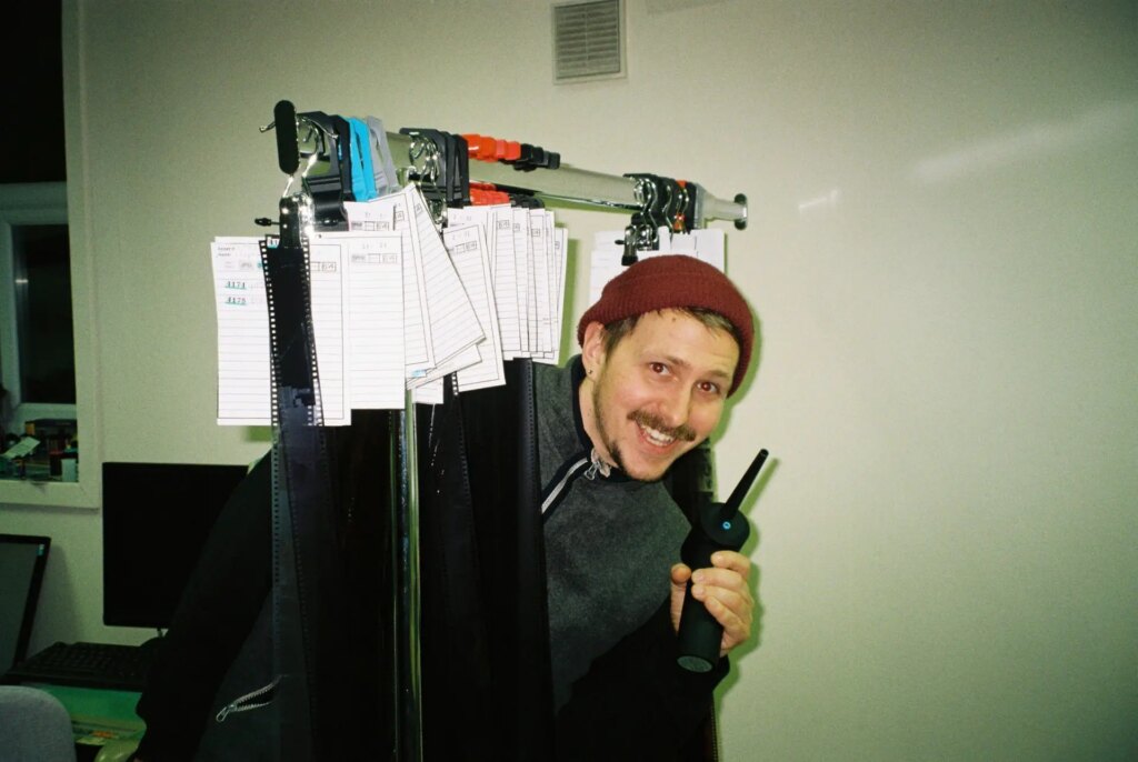 man peeking out from behind a hanger of negatives in a film lab