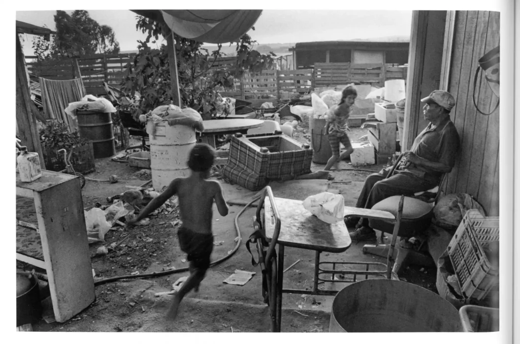 Children Playing Surrounded by Discarded Objects, Watched Over by Elderly Man
