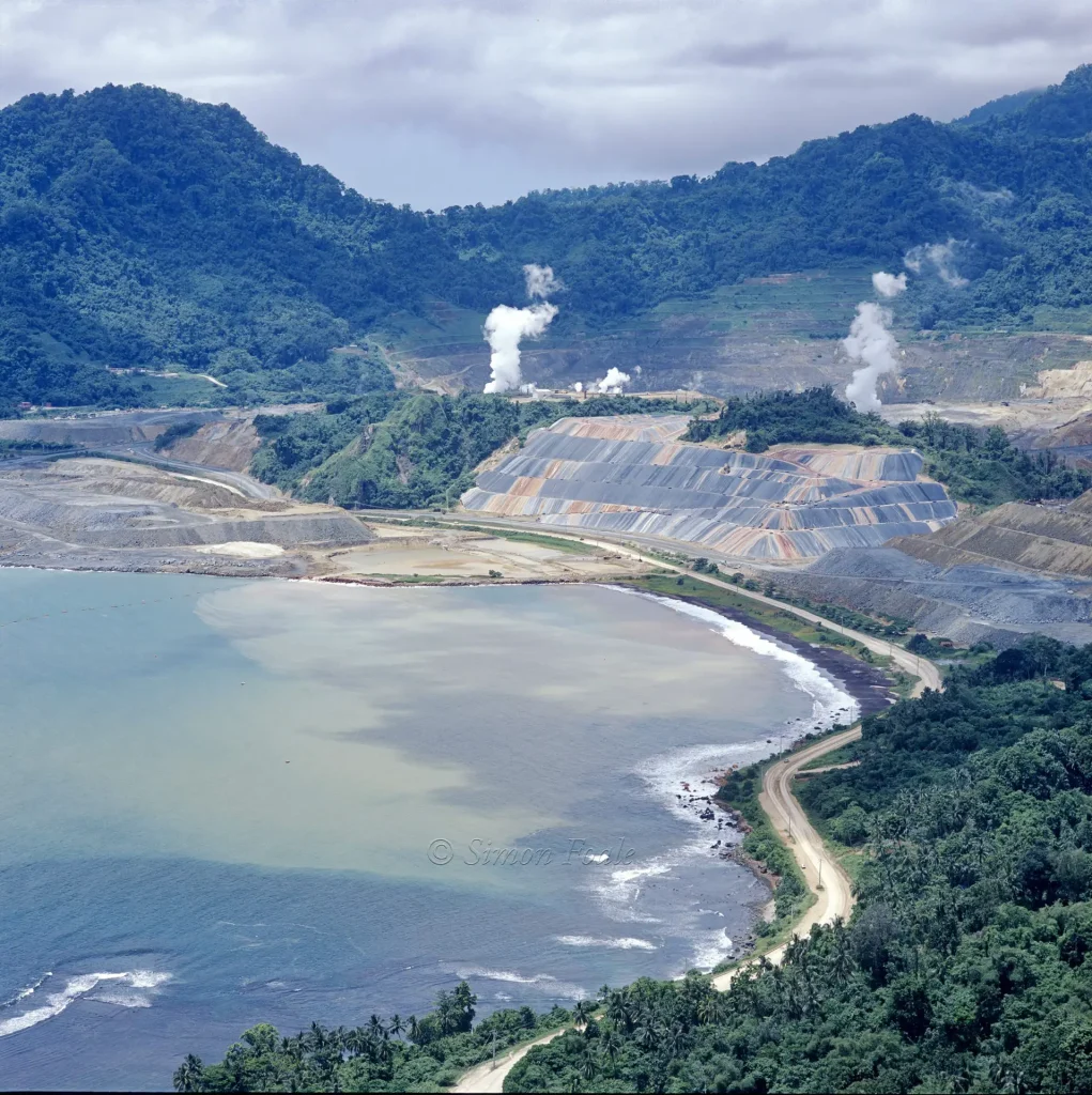 Mine site on coast of island with plastic-covered ore stockpiles.