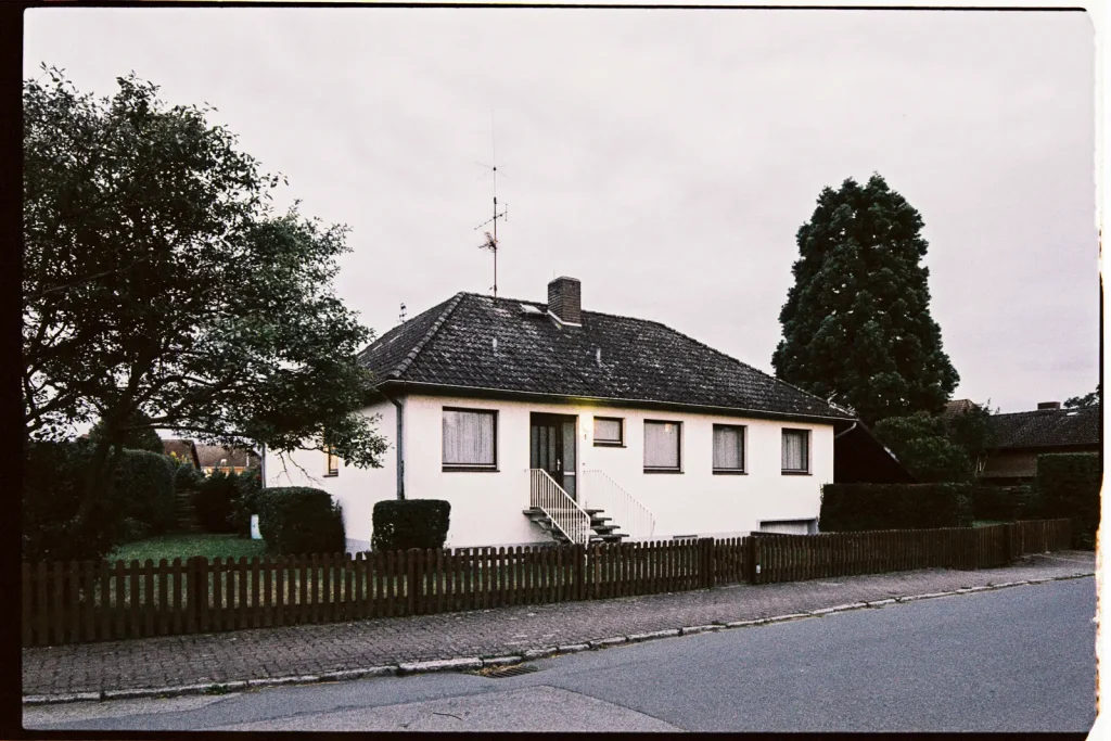 A small residential house in a suburban area, surrounded by dark trees