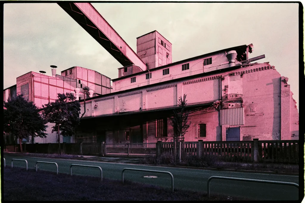 Extremly pinkish looking factory building of a cement works with a conveyor belt bridge visible above.