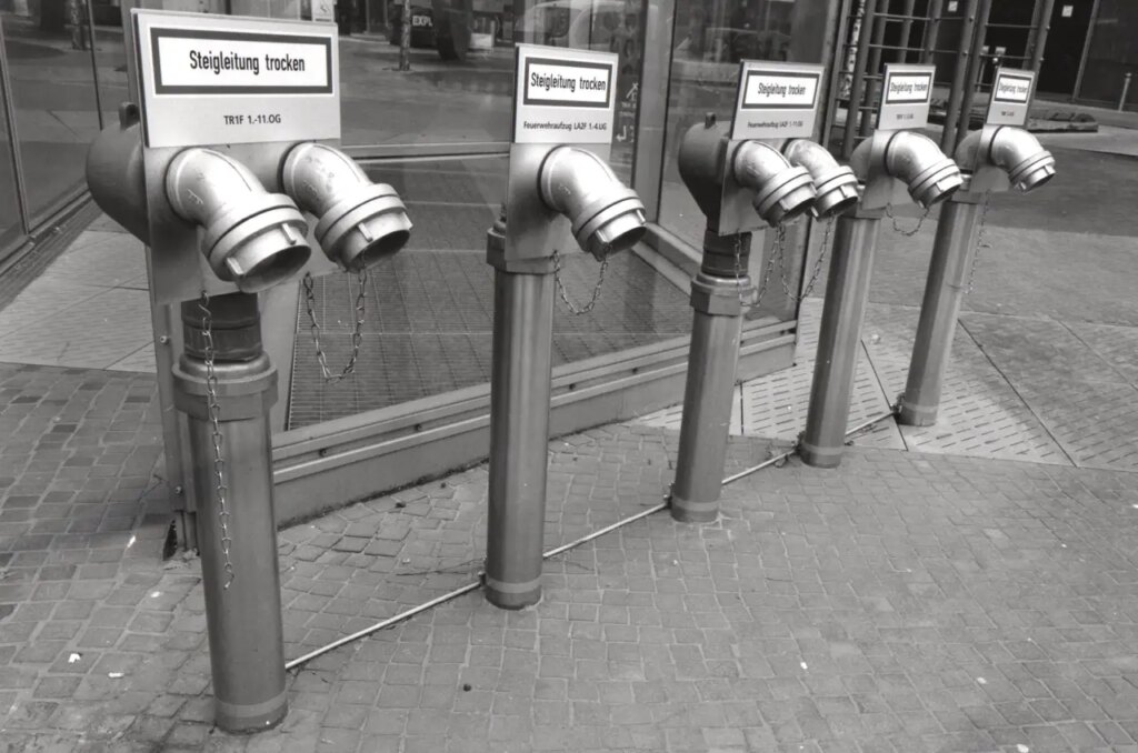 This image has a really three dimensional quality as a print with the diagonal line of pipes crossing the middle of the composition with a nice reflective pice of glass dividing fore ground and distance. It is a window and a mirror picking up some traffic reflections.